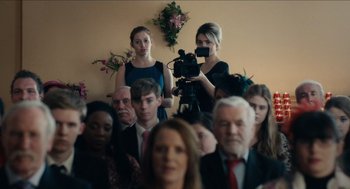 Movie still from “A Date for Mad Mary” (2016), directed by Darren Thornton – A group of people in a room with a video camera; Medium shot, Over the shoulder angle