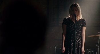 Movie still from “A Date for Mad Mary” (2016), directed by Darren Thornton – A woman standing in front of a microphone on a stage; Medium shot, Over the shoulder angle