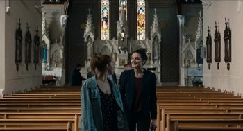 Movie still from “A Date for Mad Mary” (2016), directed by Darren Thornton – Two women are standing in front of the pews of a church; Medium shot, Low angle