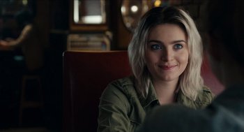 Movie still from “A Date for Mad Mary” (2016), directed by Darren Thornton – A woman sitting in a chair smiling for the camera; Close Up shot, Over the shoulder angle