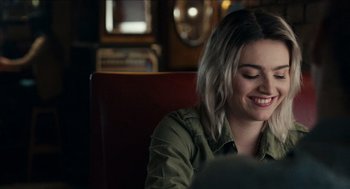 Movie still from “A Date for Mad Mary” (2016), directed by Darren Thornton – A woman sitting at a table smiling at the camera; Close Up shot, Over the shoulder angle