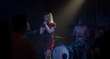 Movie still from “A Date for Mad Mary” (2016), directed by Darren Thornton – A woman singing into a microphone in front of a drum set; Medium shot, Over the shoulder angle