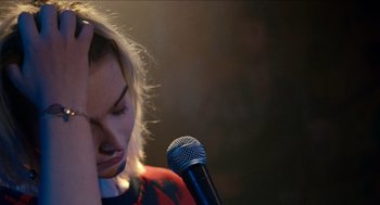 Movie still from “A Date for Mad Mary” (2016), directed by Darren Thornton – A woman with her hand on her face and a microphone in front of her face; Close Up shot, High angle