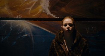 Movie still from “A Date for Mad Mary” (2016), directed by Darren Thornton – A woman wearing a fur coat standing in front of a wall; Medium shot, Low angle