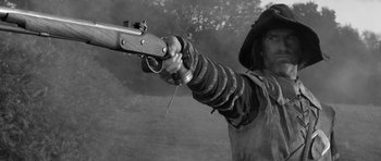 Movie still from “A Field in England” (2013), directed by Ben Wheatley – A man is holding a rifle in his hand; Medium shot, Low angle