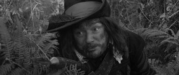 Movie still from “A Field in England” (2013), directed by Ben Wheatley – A person wearing a hat and holding something; Close Up shot, Over the shoulder angle