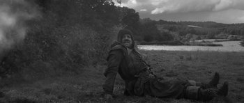Movie still from “A Field in England” (2013), directed by Ben Wheatley – A man sitting on the ground in the grass; Wide shot, High angle