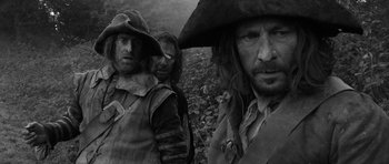 Movie still from “A Field in England” (2013), directed by Ben Wheatley – A black and white photo of three men in medieval garb; Medium shot, Low angle