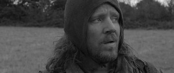 Movie still from “A Field in England” (2013), directed by Ben Wheatley – A person wearing a hooded jacket; Close Up shot, Over the shoulder angle