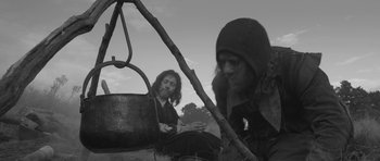 Movie still from “A Field in England” (2013), directed by Ben Wheatley – Two people sitting on a swing in a field; Medium shot, Low angle