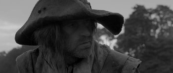 Movie still from “A Field in England” (2013), directed by Ben Wheatley – A person wearing a hat; Close Up shot, Over the shoulder angle