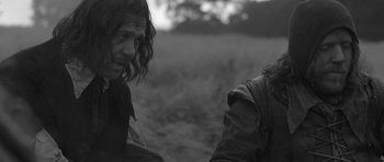 Movie still from “A Field in England” (2013), directed by Ben Wheatley – A man sitting on the ground in a grassy field; Medium shot, Over the shoulder angle