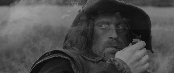 Movie still from “A Field in England” (2013), directed by Ben Wheatley – A black - and - white photo of a man with a beard; Close Up shot, Over the shoulder angle