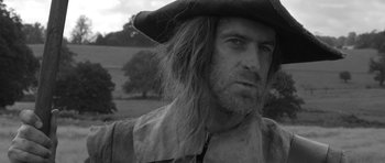 Movie still from “A Field in England” (2013), directed by Ben Wheatley – A black and white photo of a man in a pirate's hat; Close Up shot, Over the shoulder angle