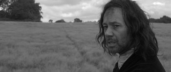 Movie still from “A Field in England” (2013), directed by Ben Wheatley – Black and white photograph of a man with long hair in a field; Close Up shot, Low angle