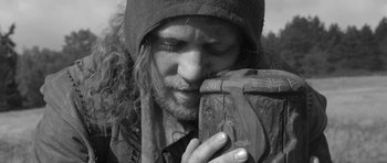 Movie still from “A Field in England” (2013), directed by Ben Wheatley – A man with long hair is holding a piece of wood in his hands; Extreme Close Up shot, Low angle