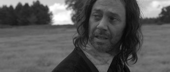 Movie still from “A Field in England” (2013), directed by Ben Wheatley – Black and white photograph of a man with long curly hair; Close Up shot, Over the shoulder angle