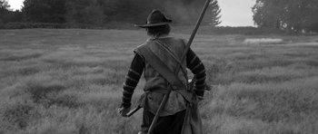 Movie still from “A Field in England” (2013), directed by Ben Wheatley – A man with a hat carrying a rifle in a field; Medium shot, Over the shoulder angle