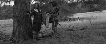 Movie still from “A Field in England” (2013), directed by Ben Wheatley – Two men dressed in medieval clothing standing in a field; Wide shot, Over the shoulder angle