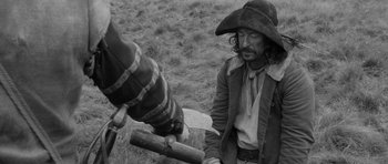 Movie still from “A Field in England” (2013), directed by Ben Wheatley – A man wearing a pirate hat and holding a gun; Medium shot, Over the shoulder angle