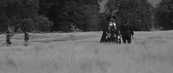 Movie still from “A Field in England” (2013), directed by Ben Wheatley – A man dressed as a cowboy standing in a grassy field; Wide shot, Low angle