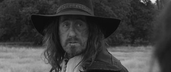 Movie still from “A Field in England” (2013), directed by Ben Wheatley – A black and white photo of a man with long hair and a hat; Close Up shot, Over the shoulder angle