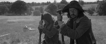 Movie still from “A Field in England” (2013), directed by Ben Wheatley – A man and a woman in pirate garb holding guns in a field; Medium shot, Low angle