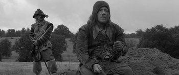 Movie still from “A Field in England” (2013), directed by Ben Wheatley – A black and white photo of a man sitting in a field; Medium shot, Low angle