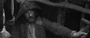 Movie still from “A Field in England” (2013), directed by Ben Wheatley – A black and white photo of a man in a pirate costume; Medium shot, Overhead angle