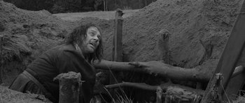 Movie still from “A Field in England” (2013), directed by Ben Wheatley – A man in a field with a bunch of dirt on the ground; Medium shot, Over the shoulder angle