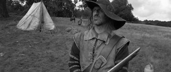 Movie still from “A Field in England” (2013), directed by Ben Wheatley – A black and white photo of a man with a hat; Medium shot, Low angle
