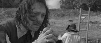 Movie still from “A Field in England” (2013), directed by Ben Wheatley – A black and white photo of a man praying; Close Up shot, Over the shoulder angle