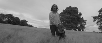Movie still from “A Field in England” (2013), directed by Ben Wheatley – A man with long dreadlocks standing in a grassy field; Medium shot, Low angle