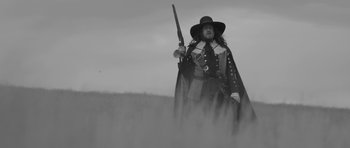Movie still from “A Field in England” (2013), directed by Ben Wheatley – A man dressed as a musketeer holding a rifle; Medium shot, Low angle
