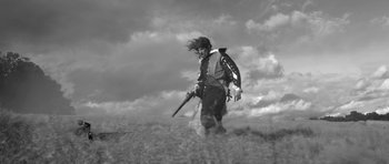 Movie still from “A Field in England” (2013), directed by Ben Wheatley – A man holding a gun while standing in a field; Wide shot, Low angle