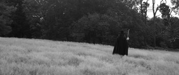 Movie still from “A Field in England” (2013), directed by Ben Wheatley – A person in a field with trees in the background; Wide shot, Low angle