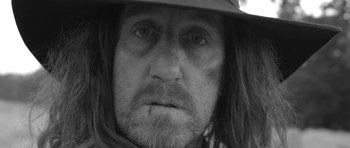 Movie still from “A Field in England” (2013), directed by Ben Wheatley – A person with long hair wearing a hat; Extreme Close Up shot, Low angle