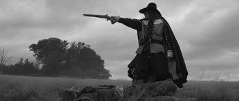 Movie still from “A Field in England” (2013), directed by Ben Wheatley – A man dressed as a musketeer aims a rifle; Wide shot, Low angle