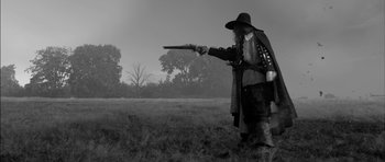 Movie still from “A Field in England” (2013), directed by Ben Wheatley – A man dressed as a pirate pointing a gun; Medium shot, Low angle