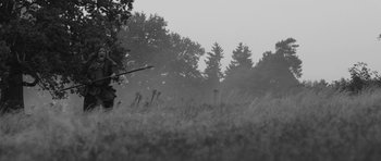 Movie still from “A Field in England” (2013), directed by Ben Wheatley – A man is standing in a field with a bow and arrow; Wide shot, Over the shoulder angle