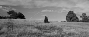 Movie still from “A Field in England” (2013), directed by Ben Wheatley – A man in a long black cape holding a sword in a grassy field; Wide shot, Low angle