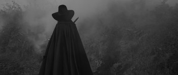 Movie still from “A Field in England” (2013), directed by Ben Wheatley – A woman in a long black dress and a hat holding a sword; Medium shot, Low angle