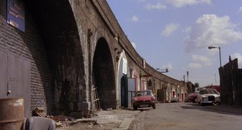Movie still from “A Fish Called Wanda” (1988), directed by Charles Crichton – An old car is parked on the side of the road; Extreme Wide shot, Low angle