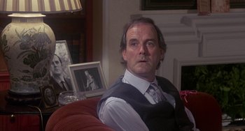 Movie still from “A Fish Called Wanda” (1988), directed by Charles Crichton – A man sitting on top of a red couch in a living room; Close Up shot, Over the shoulder angle