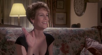 Movie still from “A Fish Called Wanda” (1988), directed by Charles Crichton – A woman sitting on top of a couch waving at the camera; Medium shot, Over the shoulder angle