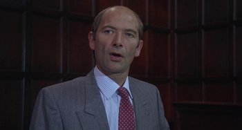 Movie still from “A Fish Called Wanda” (1988), directed by Charles Crichton – A man in a suit and tie standing in front of a wooden wall; Close Up shot, Low angle