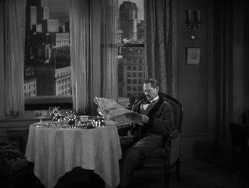 Movie still from “A Free Soul” (1931), directed by Clarence Brown – A man sitting at a table reading a newspaper in front of a window; Wide shot, High angle