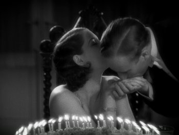 Movie still from “A Free Soul” (1931), directed by Clarence Brown – A man and a woman kissing in front of a cake; Close Up shot, High angle