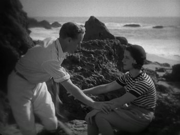 Movie still from “A Free Soul” (1931), directed by Clarence Brown – A man and a woman sitting on a rock near the ocean; Medium shot, High angle