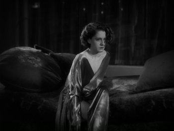 Movie still from “A Free Soul” (1931), directed by Clarence Brown – A woman sitting on top of a couch in front of a window; Medium shot, High angle